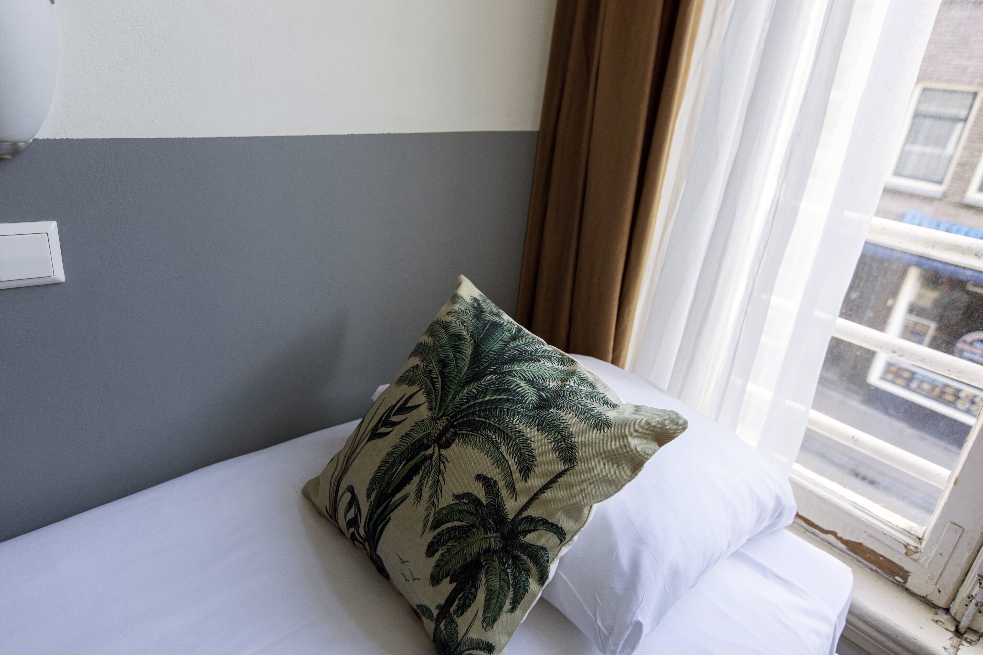 A bed with a white pillow and a pillow with a palm tree pattern.