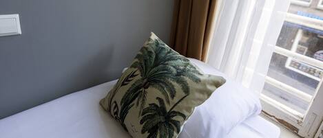 A bed with a white pillow and a pillow with a palm tree pattern.