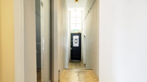 Ein schmaler Flur mit Holzboden, einer schwarzen Tür mit Fenster und einem grünen Fluchtzeichen.