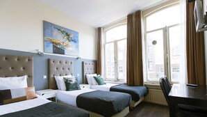 Ein Hotelzimmer mit zwei Betten, einem großen Fenster mit Vorhängen, einem Gemälde an der Wand und einem Schreibtisch mit Stuhl.