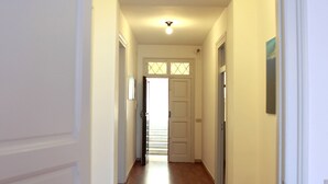 Un pasillo con suelo de madera, paredes blancas y una puerta al final.