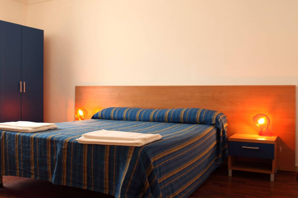 Une chambre à coucher comprenant un lit, des tables de chevet, une armoire et un luminaire suspendu.