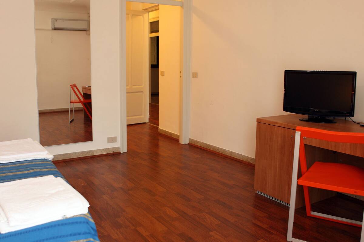Une chambre avec un lit, un bureau avec une télévision et une chaise.