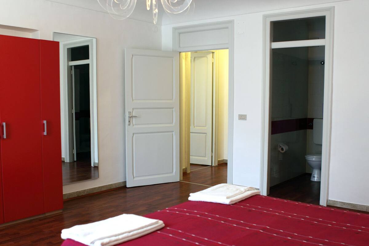 Une chambre à coucher avec une couvre-lit rouge, une porte blanche et un miroir.