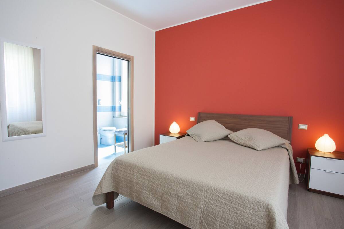 Une chambre à coucher comprenant un lit, des lampes de chevet, une fenêtre et une porte donnant sur un balcon.