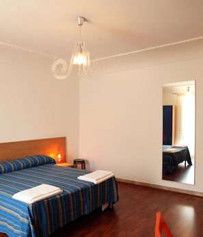Une chambre d’hôtel avec un lit, une table de chevet, une chaise, un miroir et un lustre.