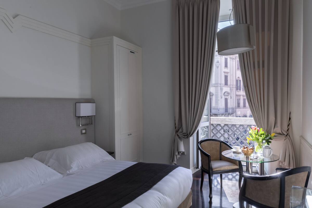 A hotel room with a bed, a small table with a vase of flowers, and a chair.