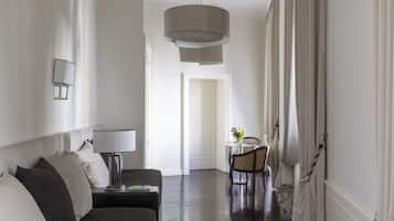 A hotel room with a dark wood floor, a sofa, a table with chairs, and a large hanging light fixture.