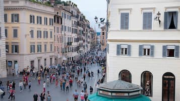 A bustling street with historic buildings, a green-roofed kiosk, and a storefront with 'Valentino' signage.