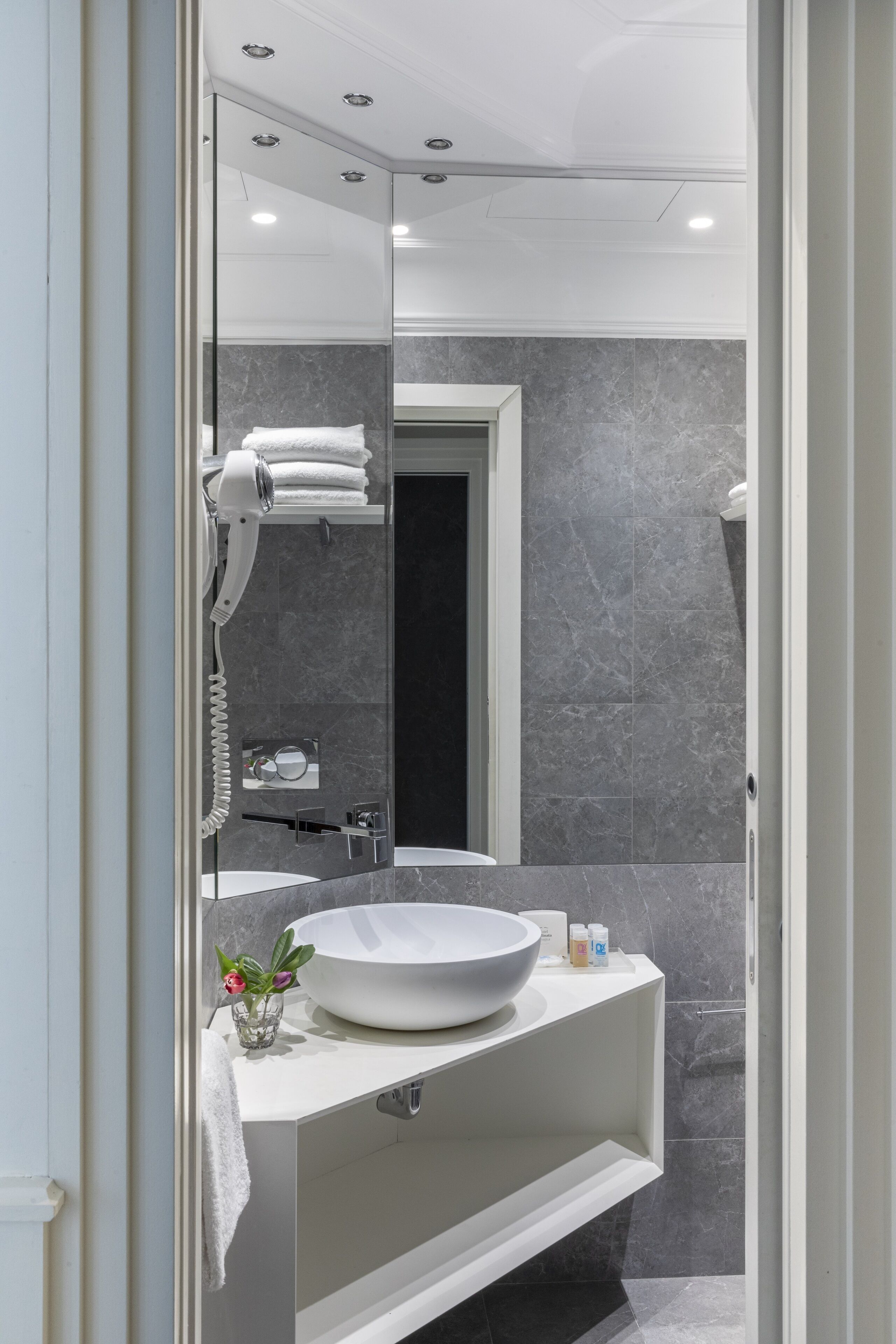 Un baño moderno con un espejo grande, un lavamanos blanco y un secador de pelo.