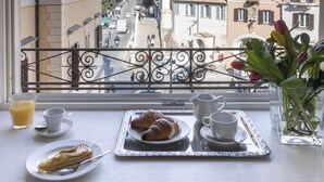 A balcony with a table set for breakfast, overlooking a street with historic buildings and a prominent tower. - Hotel Scalinata di Spagna (Rome)