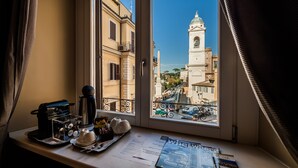 A window view of a historic building with a bell tower, a balcony with a metal railing, and a table with breakfast items and a magazine. - Hotel Scalinata di Spagna (Rome)