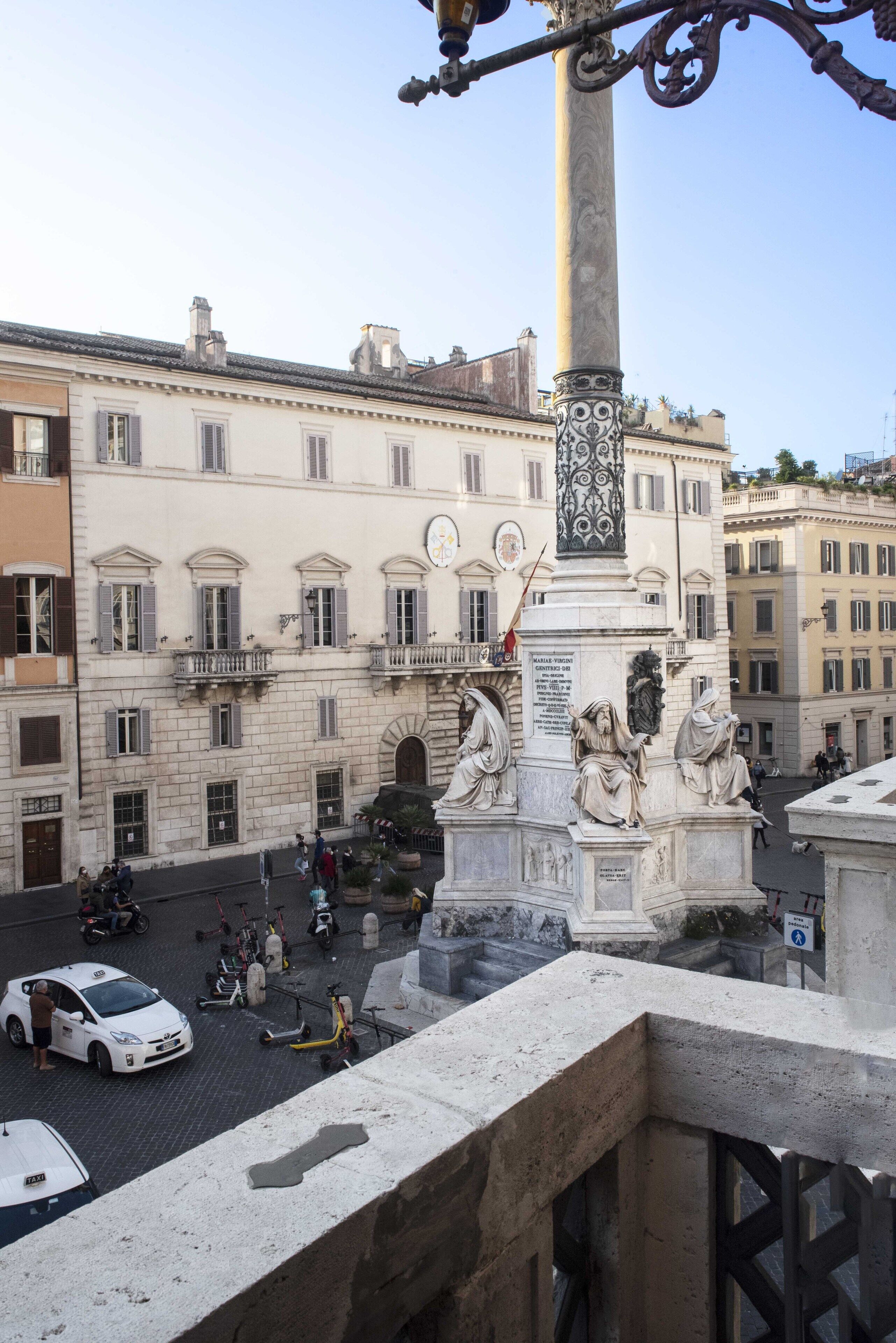 A historic square with a central monument featuring statues, surrounded by classical architecture.