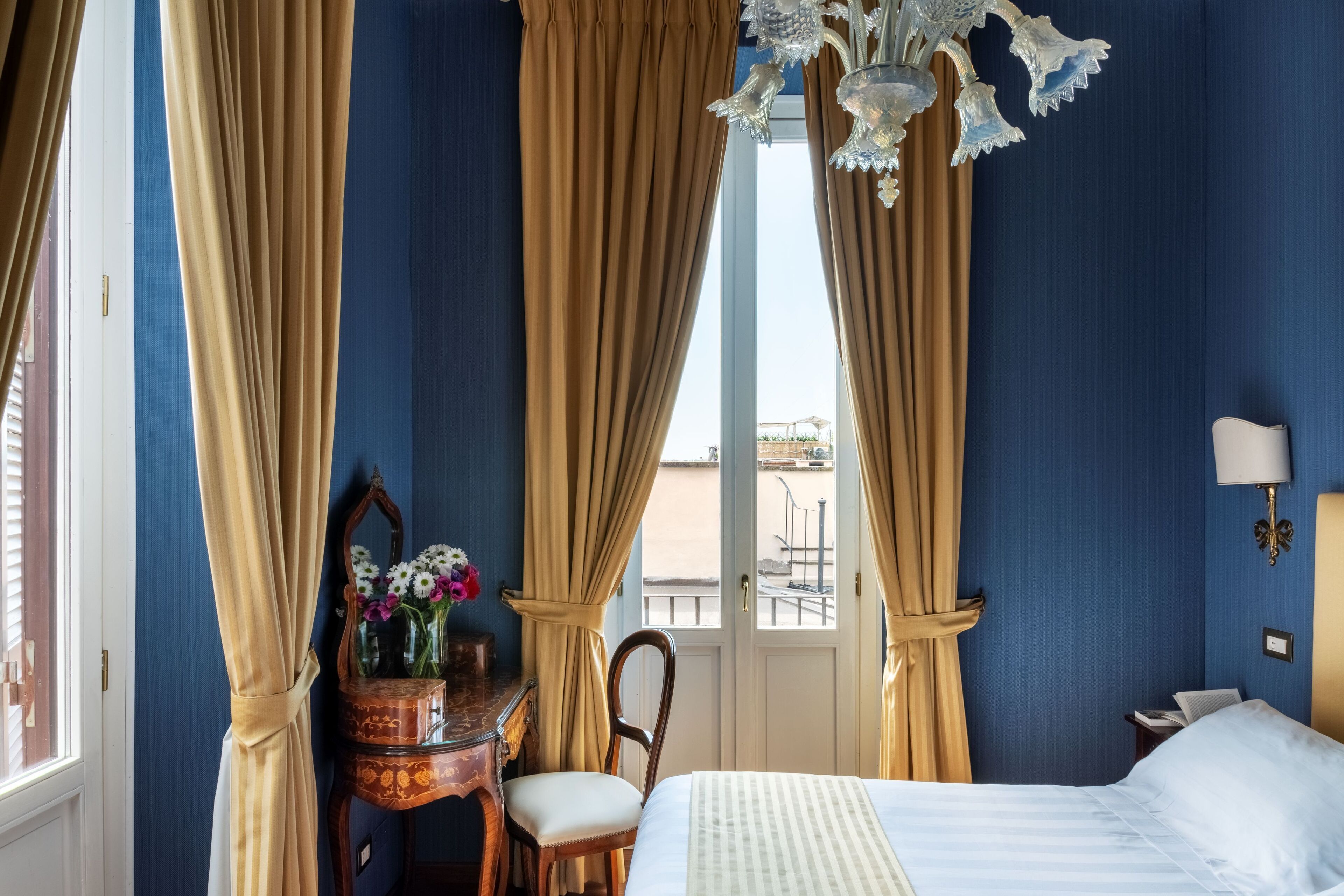 A hotel room with a bed, a desk with a mirror, a chair, and a window with curtains.