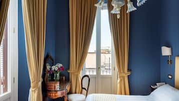 A hotel room with a bed, a desk with a mirror, a chair, and a window with curtains.
