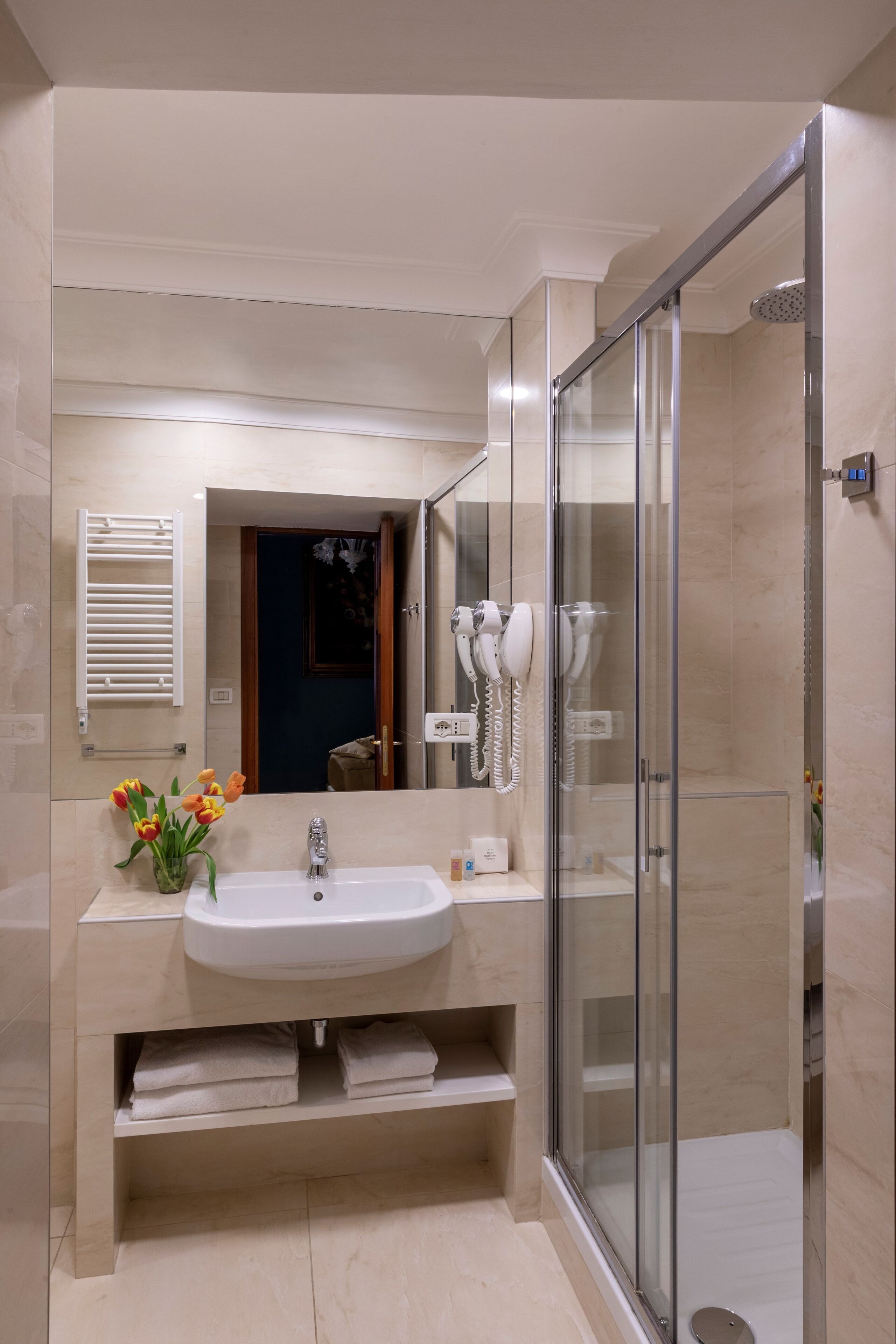 Un baño moderno con ducha envuelta en vidrio, un lavamanos con espejo y un perchero para toallas.