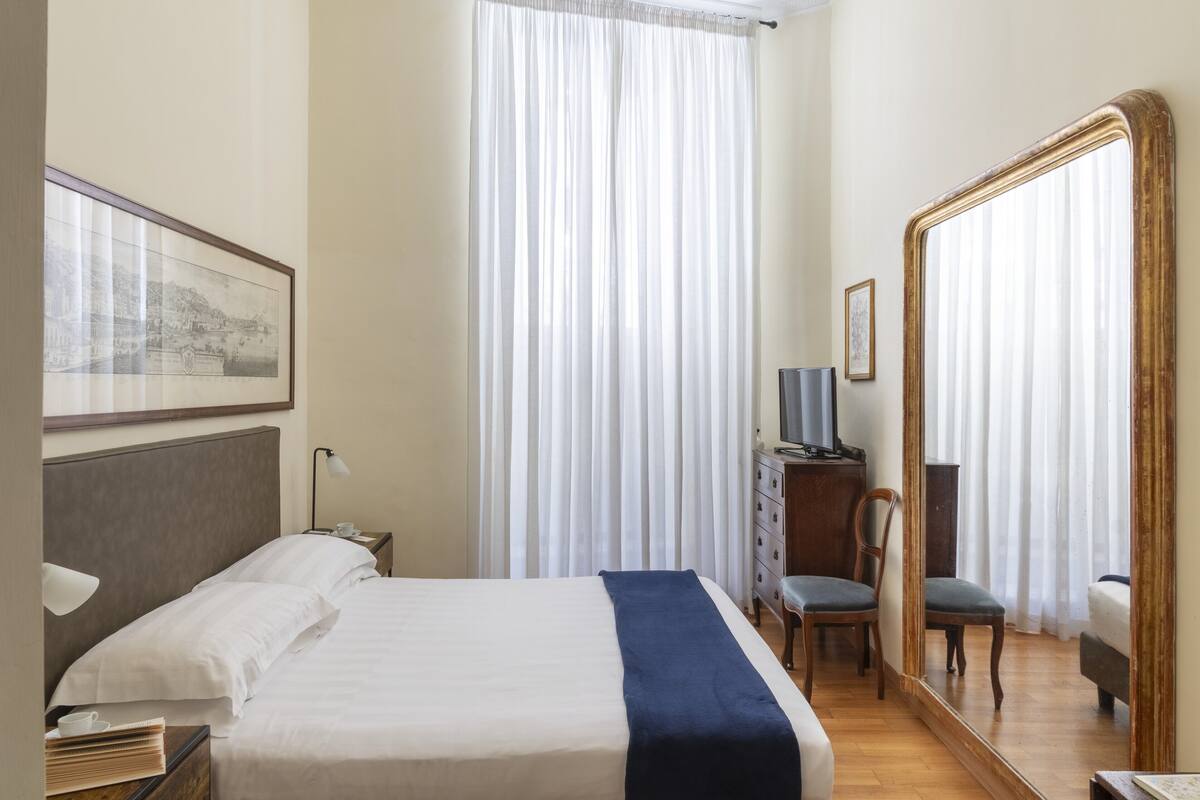 A hotel room with a bed, a chair, a dresser, a TV, and a large mirror.