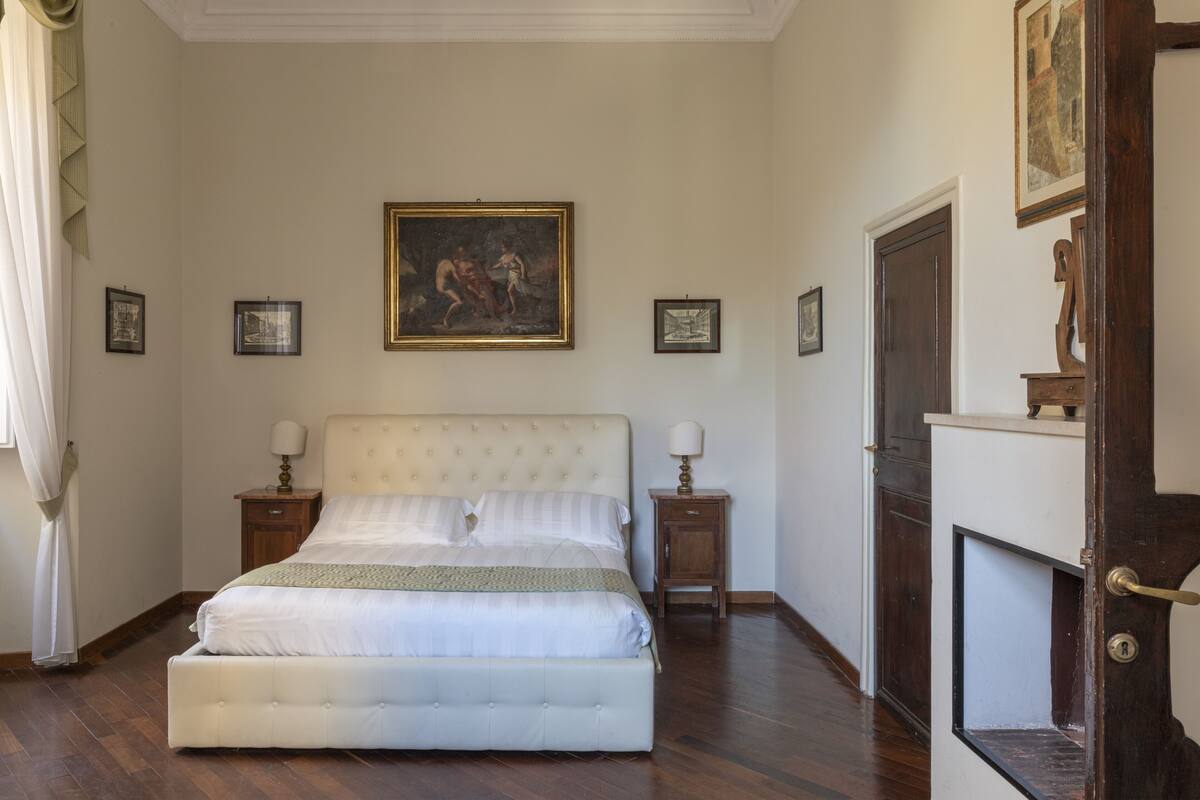 A bedroom with a large bed, two bedside tables with lamps, a painting on the wall, and a wooden cabinet.