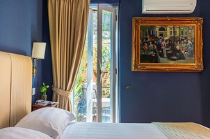 Una camera d'albergo con un letto, un comodino con una lampada, una finestra con tende e un quadro appeso al muro.
