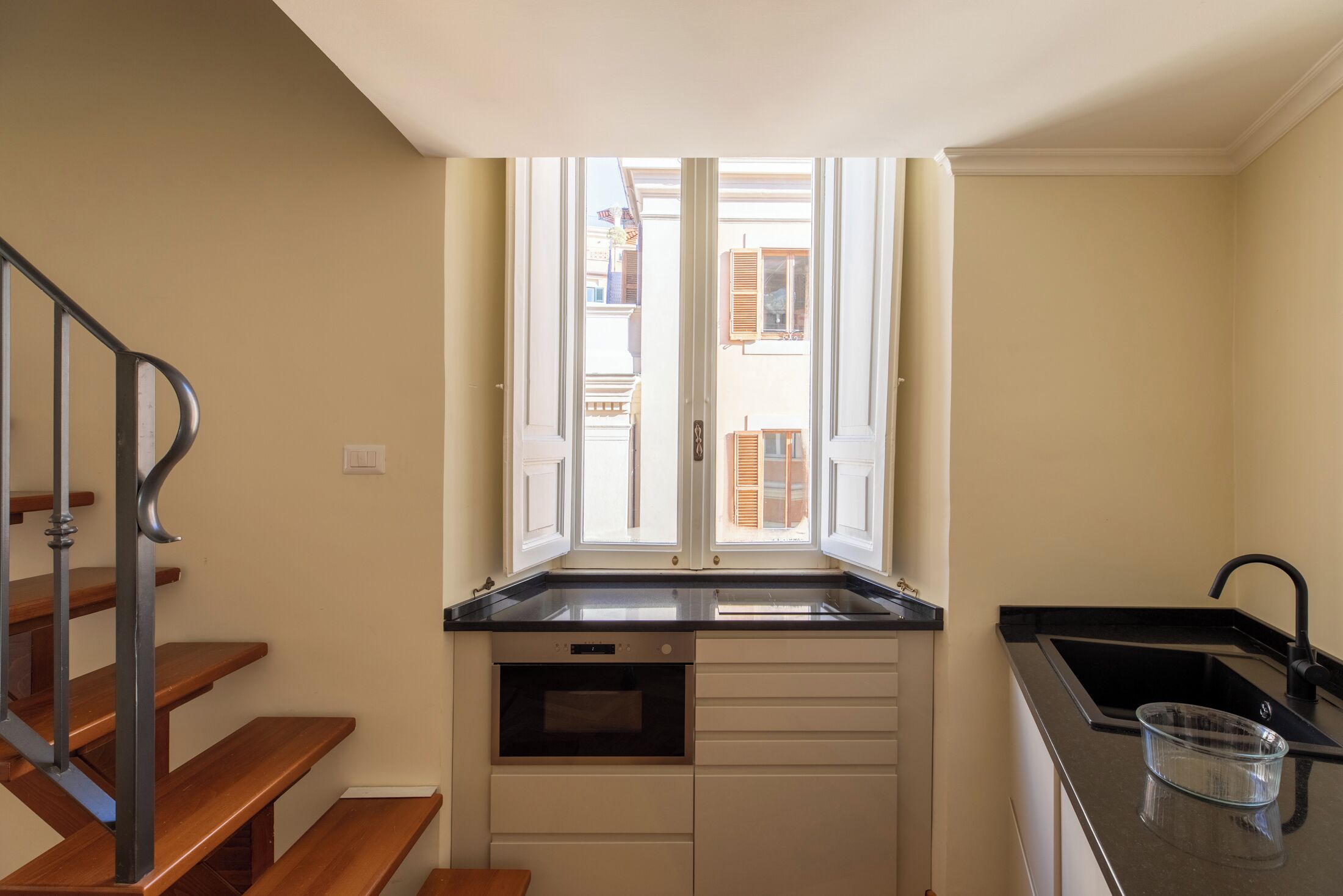 A compact kitchen with a window, built-in oven, and a sink.