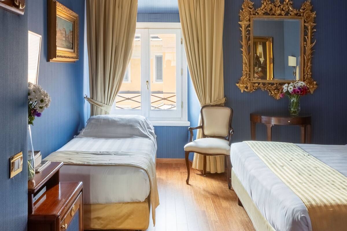 A hotel room with two beds, a wooden dresser, a chair, a mirror, and a window with curtains.