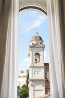 Vista attraverso una finestra con tende bianche, che mostra un edificio storico con un campanile e una cupola.
