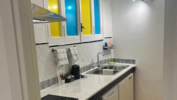 Una cocina con armarios blancos, un microondas negro, lavavajillas, un lavabo y un respuesto de azulejos.