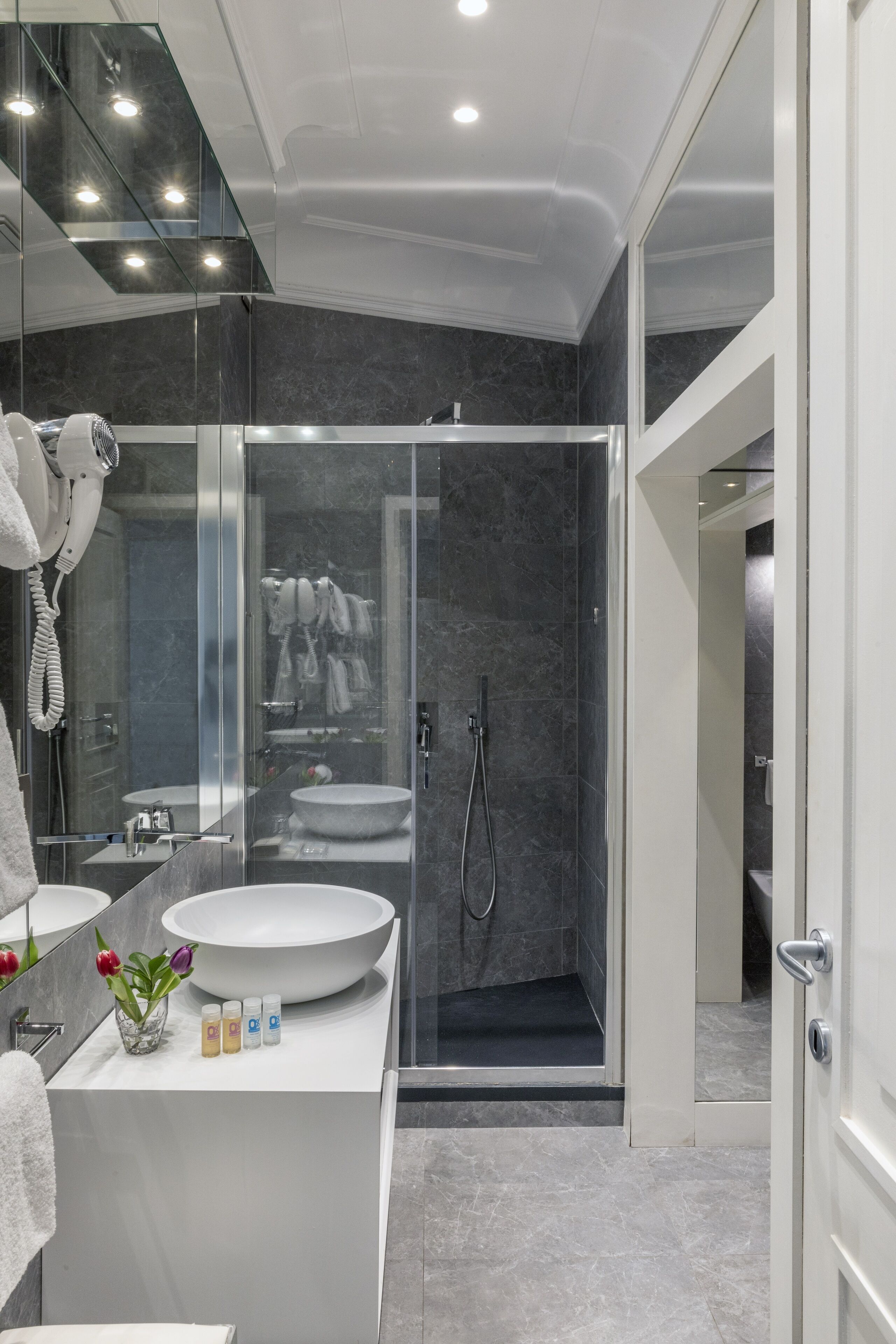 A modern bathroom with a large mirror, two sinks, a glass shower enclosure, and a walk-in shower.