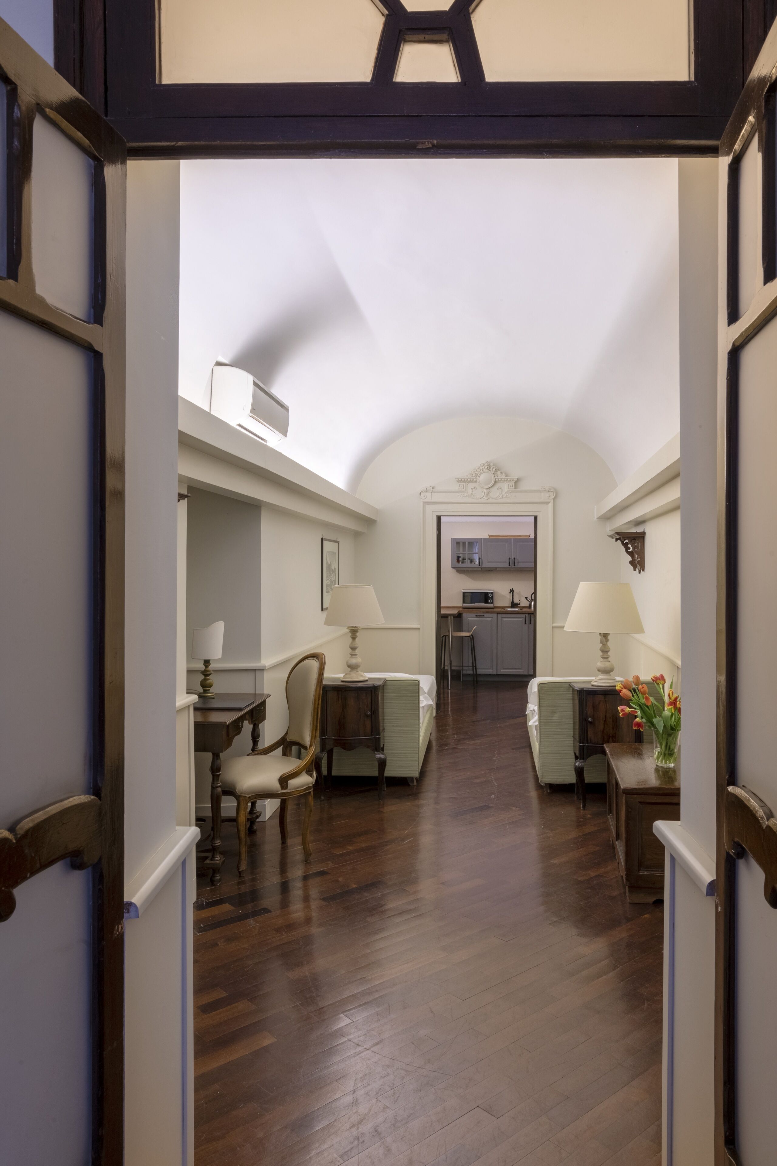 An interior view of a hallway leading to a kitchen and dining area with wooden flooring and furniture.