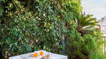 Un pequeño espacio exterior con comedor, una mesa y dos sillas, rodeado de abundante vegetación y un techo blanco.