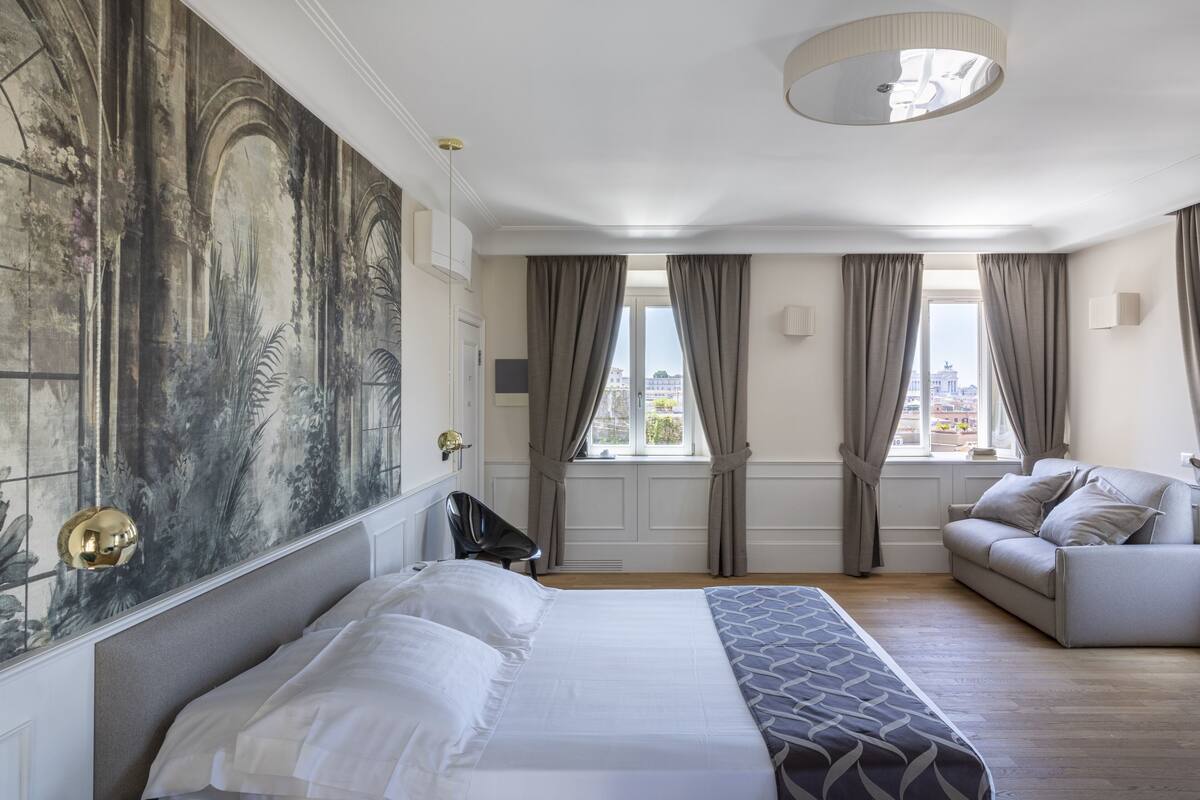 A modern hotel room with a large bed, a sofa, and a view of the city.
