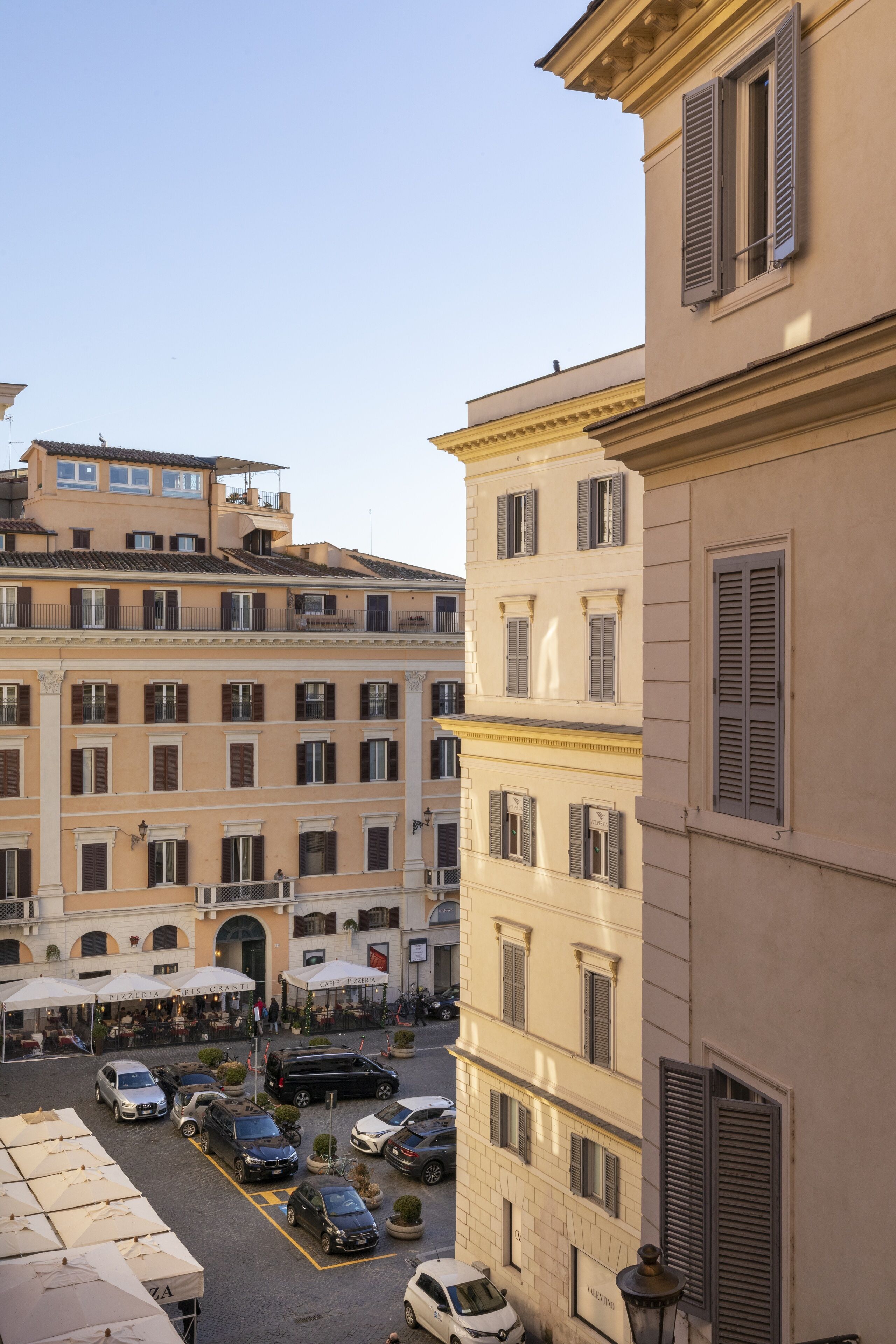 Une cour intérieure où sont garées plusieurs voitures, avec des espaces de repos en plein air et un bâtiment à l’architecture classique.