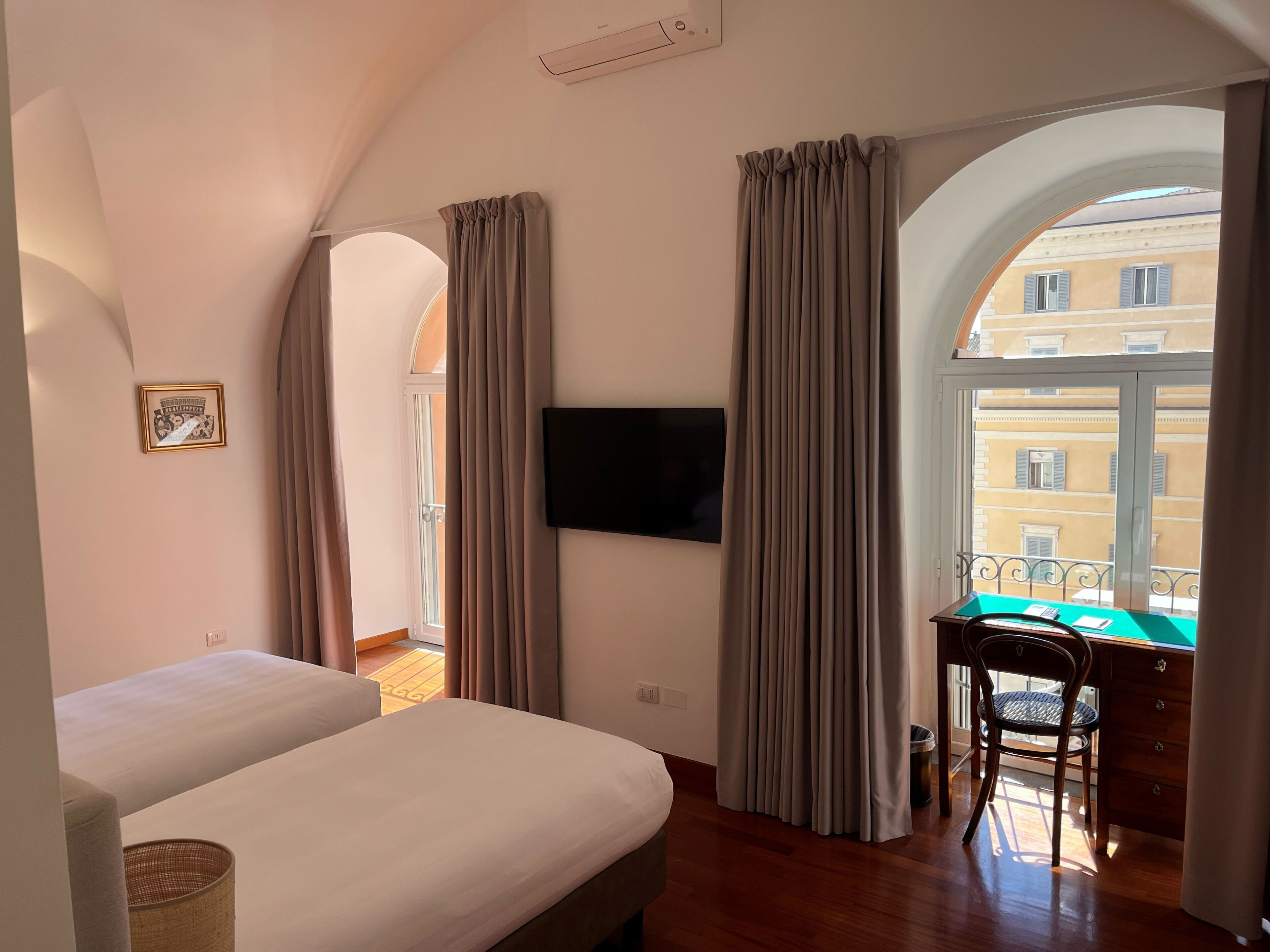 A room with a bed, a desk with a chair, a TV, and a window with curtains.