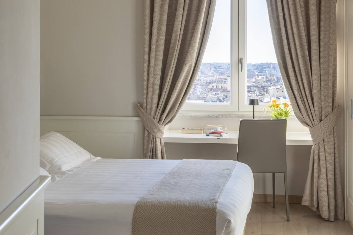 A hotel room with a bed, a desk, and a window with curtains.