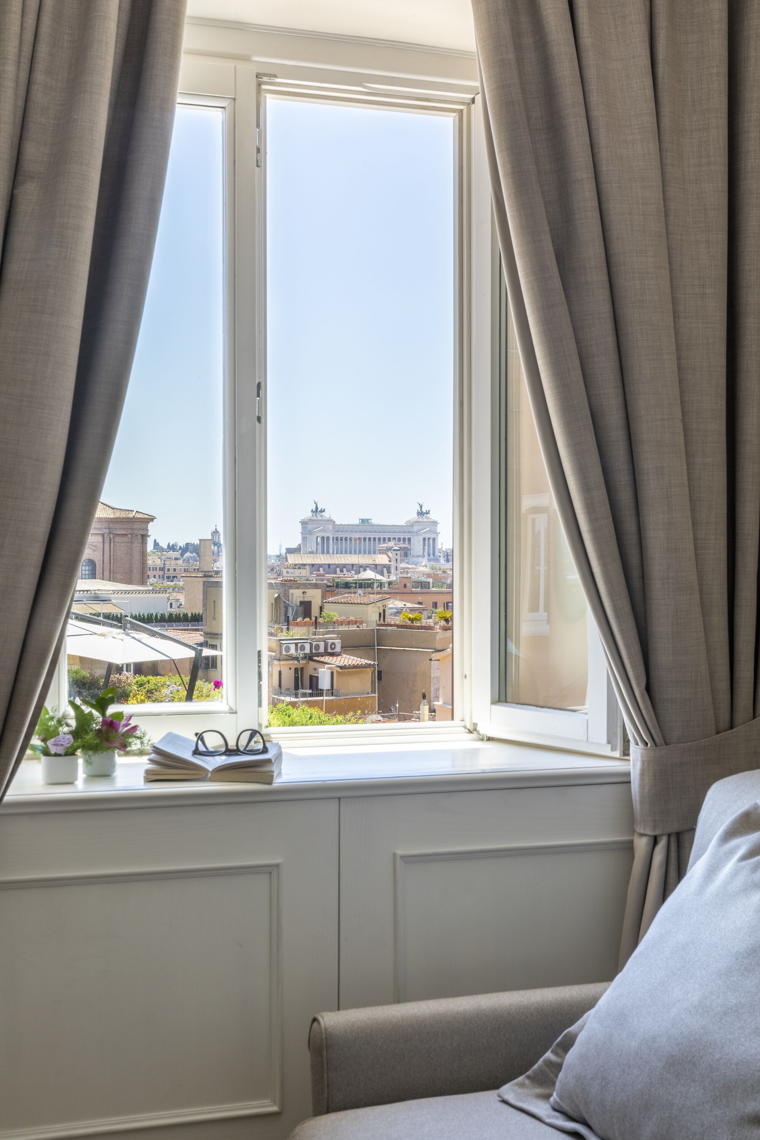 A room with a window overlooking a cityscape, a sofa, and a small table with a book and glasses.