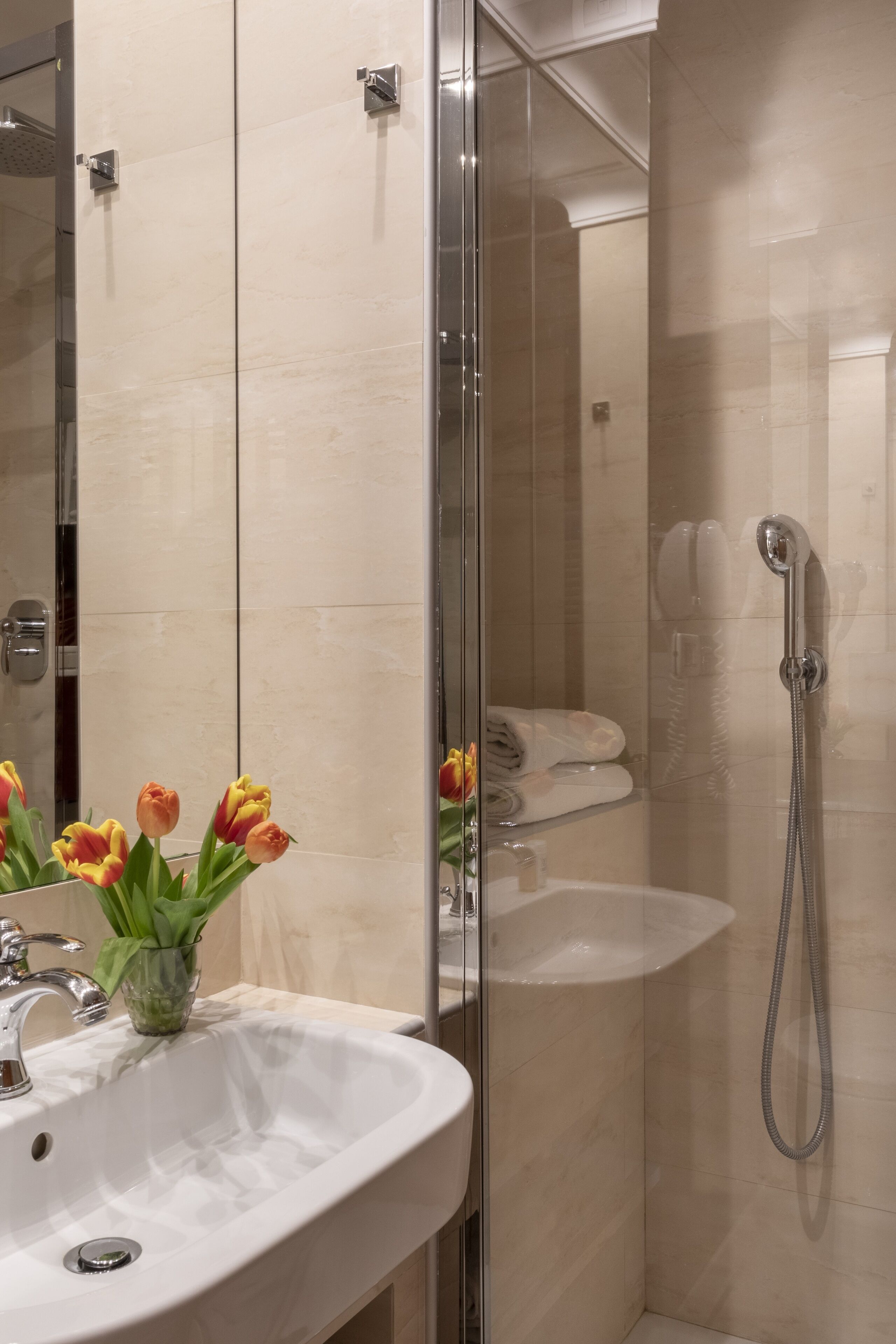 A modern bathroom with a glass shower enclosure, a white sink, and a vase of tulips.