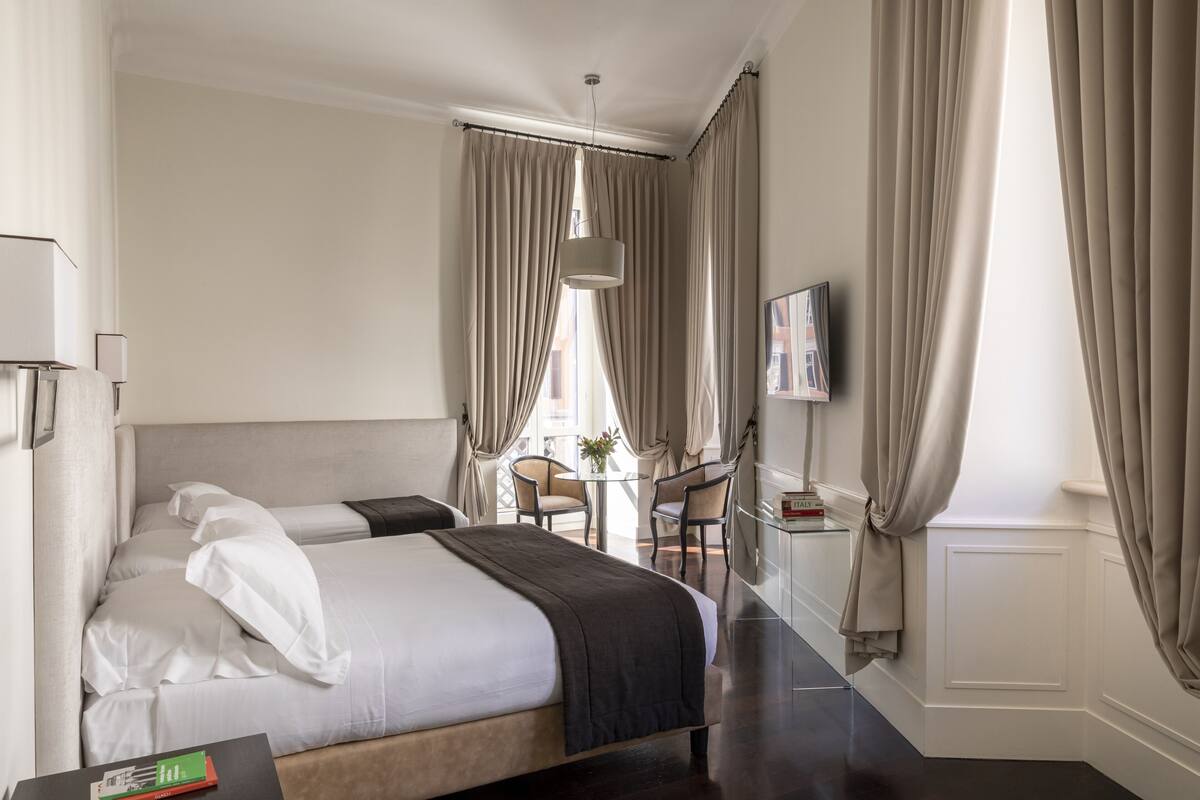 A hotel room with a bed, a desk, a chair, a TV, and a window with curtains.