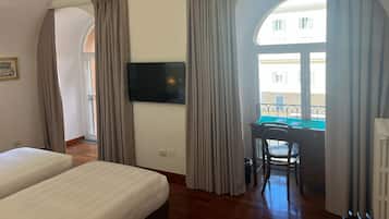 Habitación de hotel con dos camas, un escritorio, una silla, un televisor y un balcón con cortinas.
