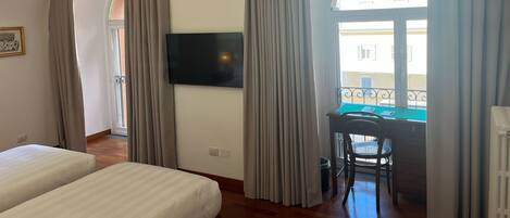 A hotel room with two beds, a desk, a chair, a TV, and a balcony with curtains.