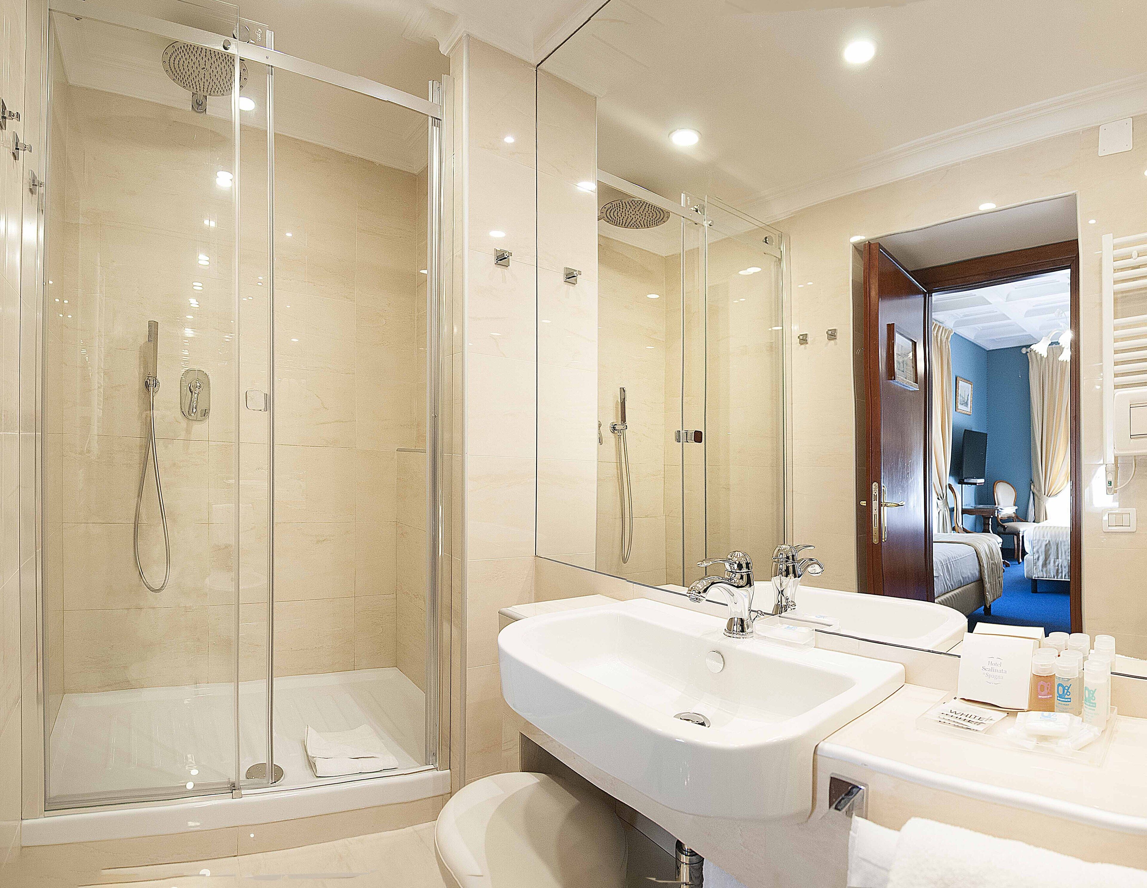 Une salle de bain d’hôtel avec une douche à parois de verre, un meuble-lavabo à deux vasques et un miroir.
