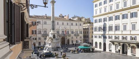 Une place publique avec un monument central, des bâtiments qui l’entourent et un fourgon rouge garé à proximité.