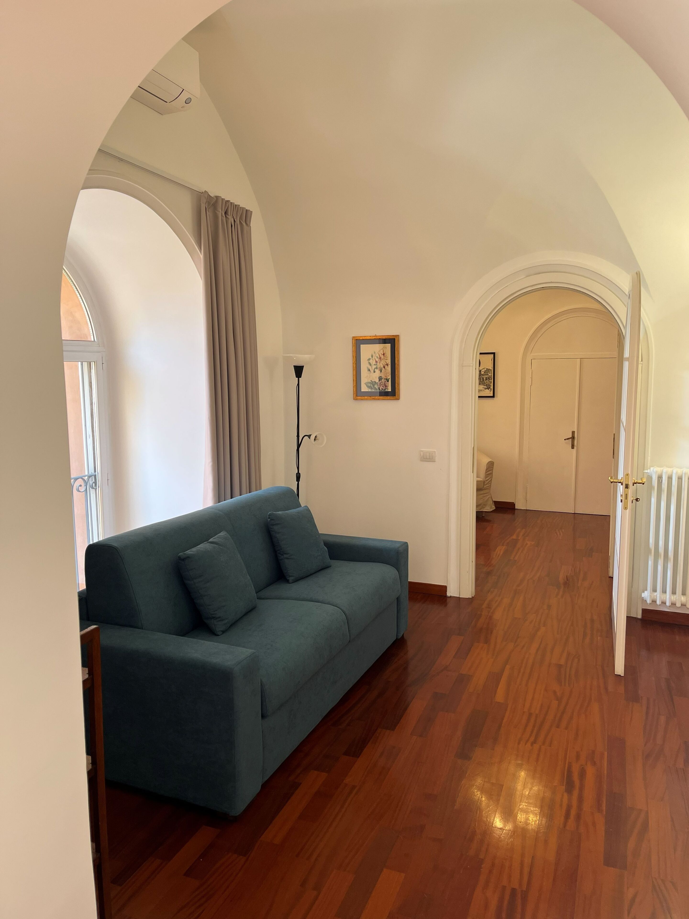 A room with a sofa, wooden flooring, an arched doorway, and a framed picture on the wall.