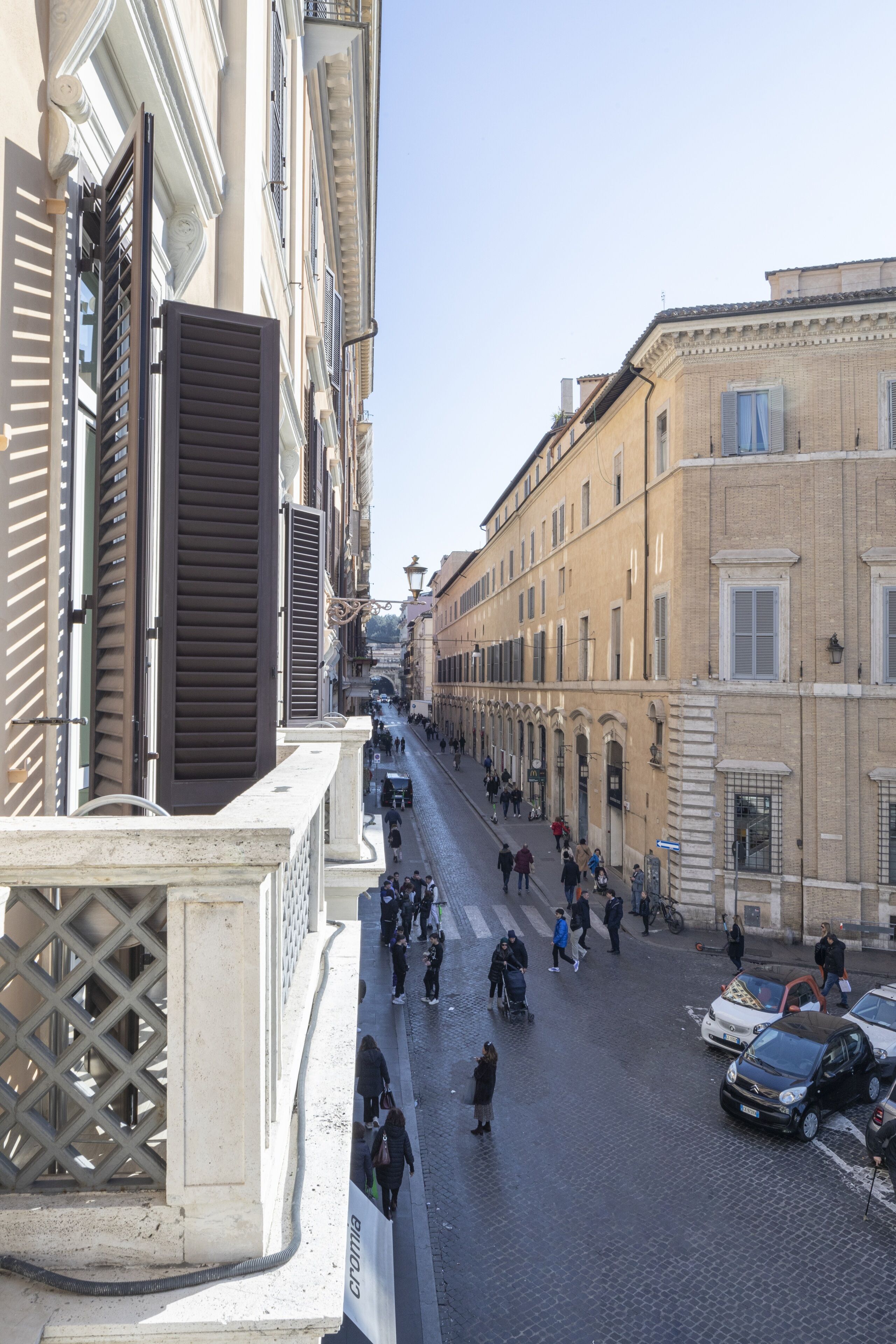 A cobblestone street lined with historic buildings, a pedestrian walkway, and parked cars.