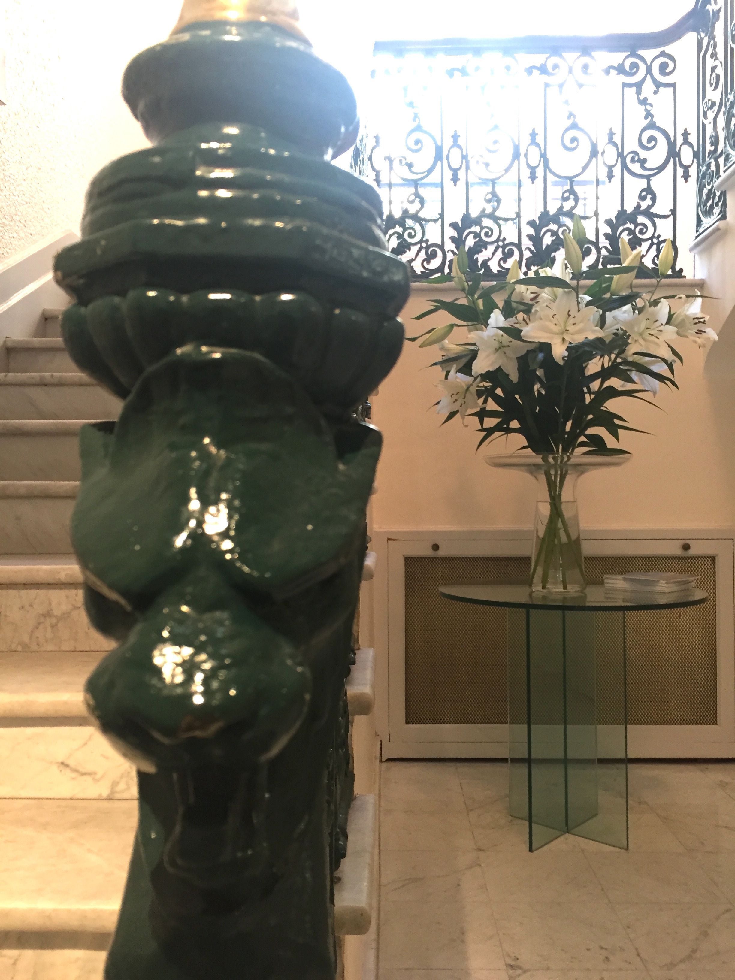 Een trap met een groen, sierlijk hekwerk en een vaas witte bloemen op een glazen tafel.