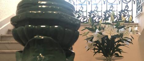 Una escalera con barandilla verde y decorativa, y un jarrón de flores blancas sobre una mesa de vidrio.