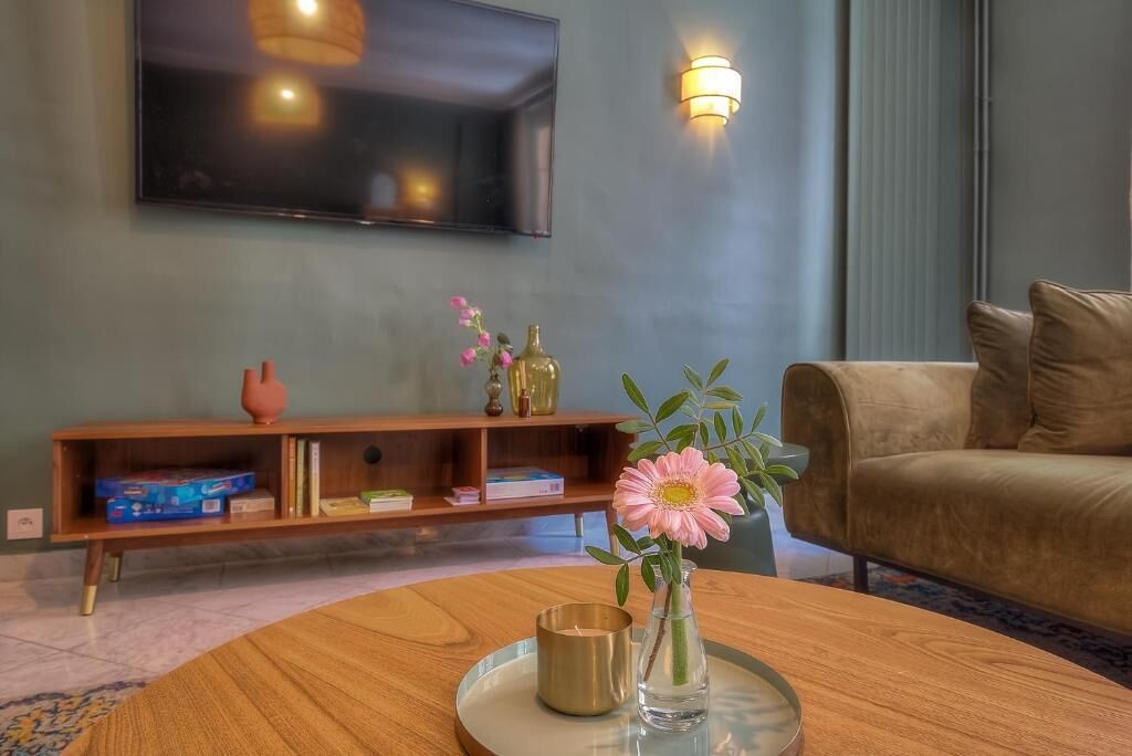 A living room with a sofa, a coffee table with a vase and candle, a TV mounted on the wall, and a bookshelf with books and decorative items.