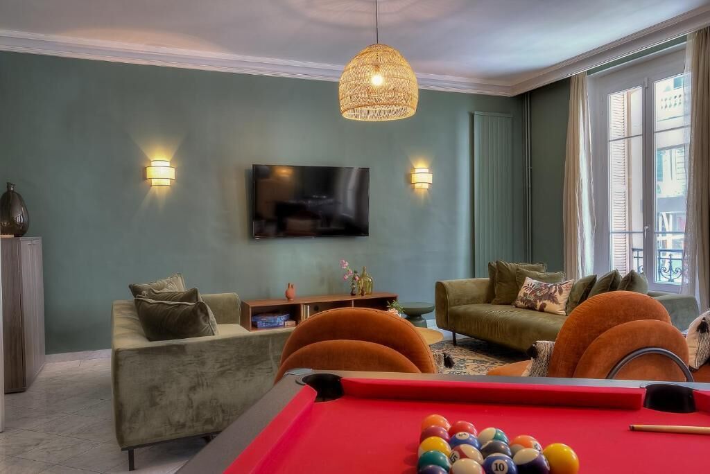 Un salon comprenant une table de billard, deux canapés, un téléviseur et une grande fenêtre.