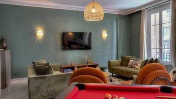 Un salon comprenant une table de billard, deux canapés, un téléviseur et une grande fenêtre.