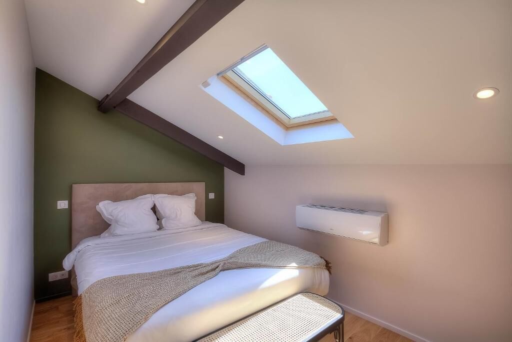 A bedroom with a skylight, a bed, a wall-mounted air conditioner, and a wooden floor.