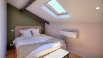 A bedroom with a skylight, a bed, a wall-mounted air conditioner, and a wooden floor.